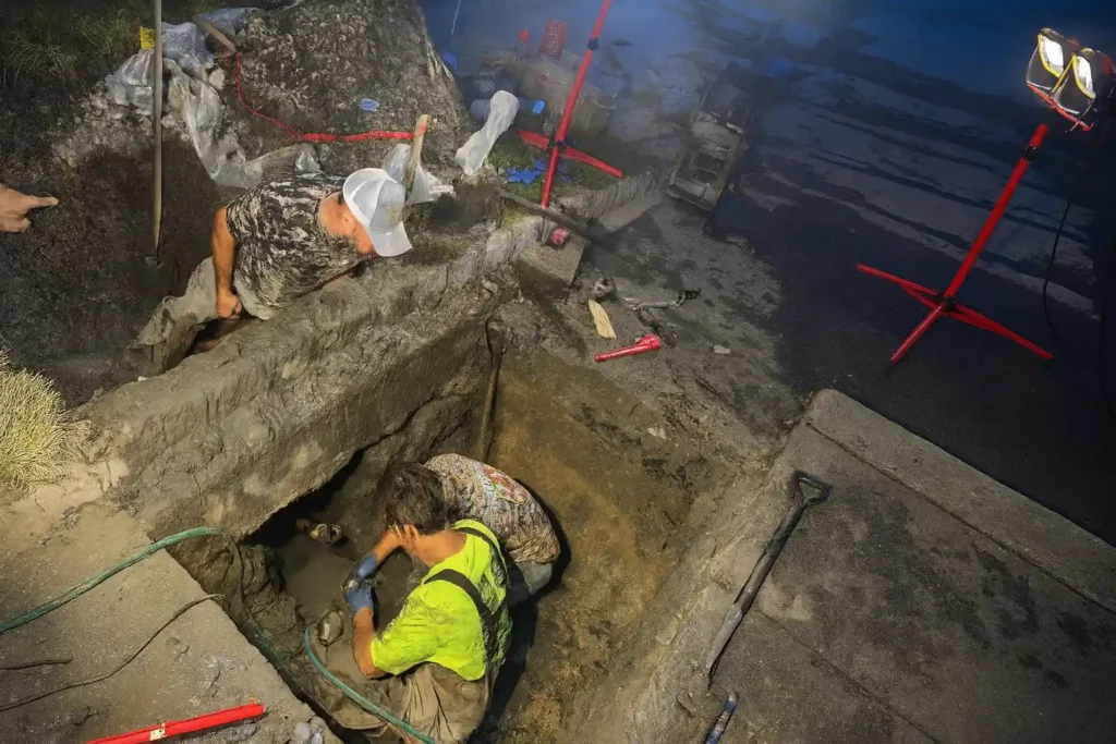Collapsed Drain Repair in Evesham NJ Workers repairing an exposed sewer line after a collapsed drain issue in Evesham NJ, using tools inside a freshly dug excavation.