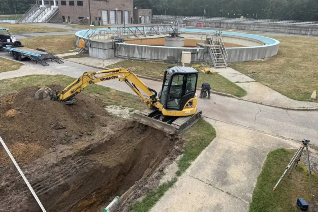 Excavator digging a deep trench at a commercial facility during a drain excavation project in Evesham NJ to expose buried drainage lines