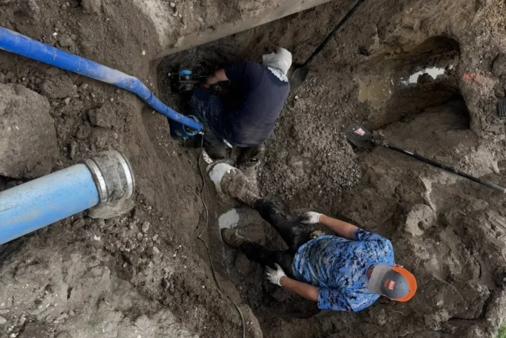 Technicians performing drain pipe replacement in Evesham NJ, working inside an excavated trench to access and repair a damaged underground pipe.