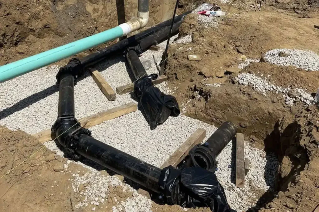 A commercial excavation site in Evesham NJ with exposed drain lines staged for relining, showing gravel bedding and pipe layout around a large tank.