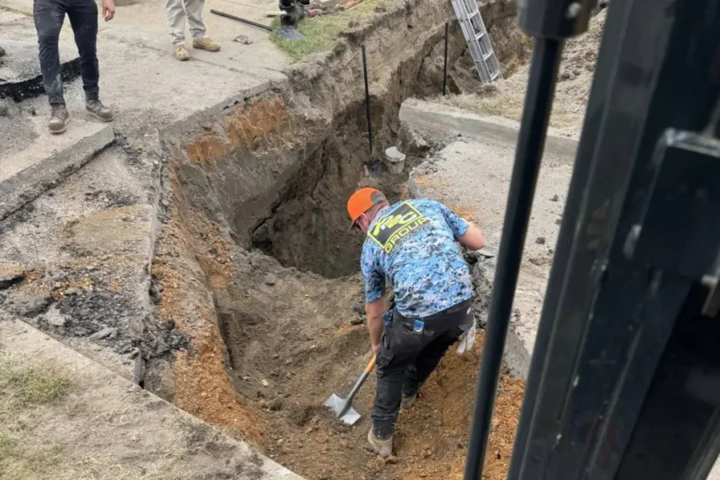 Workers excavating a deep trench to expose buried drainage lines as part of a drain tracing project in Evesham NJ.