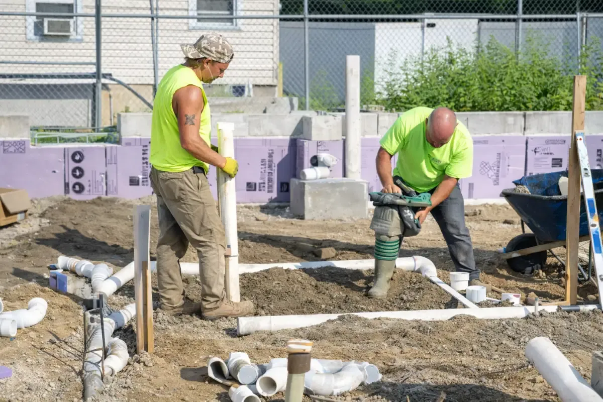 How Much Does Grease Trap Cleaning Cost? Two workers installing drain pipes at a commercial building foundation