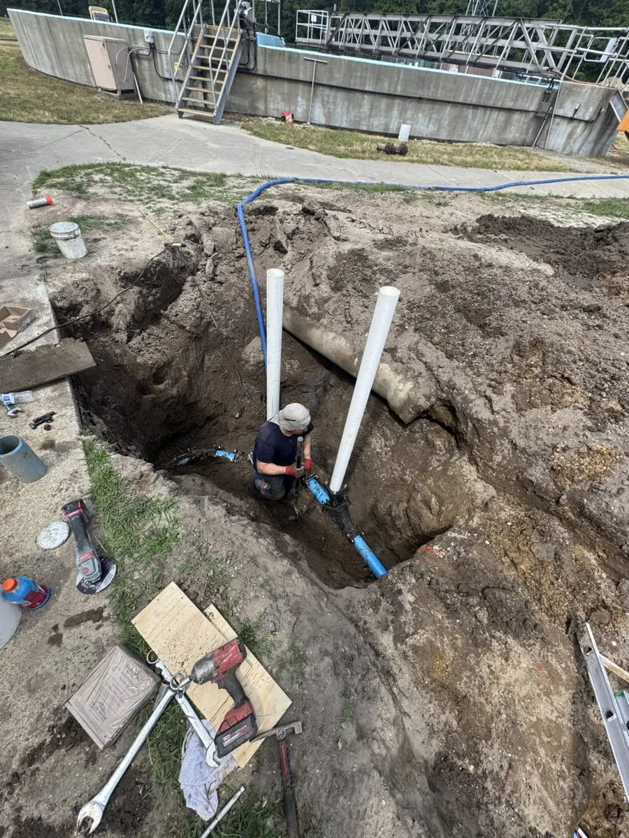 How Much Does Grease Trap Cleaning Cost? Worker in a deep excavation beside two vertical pipes at a commercial property