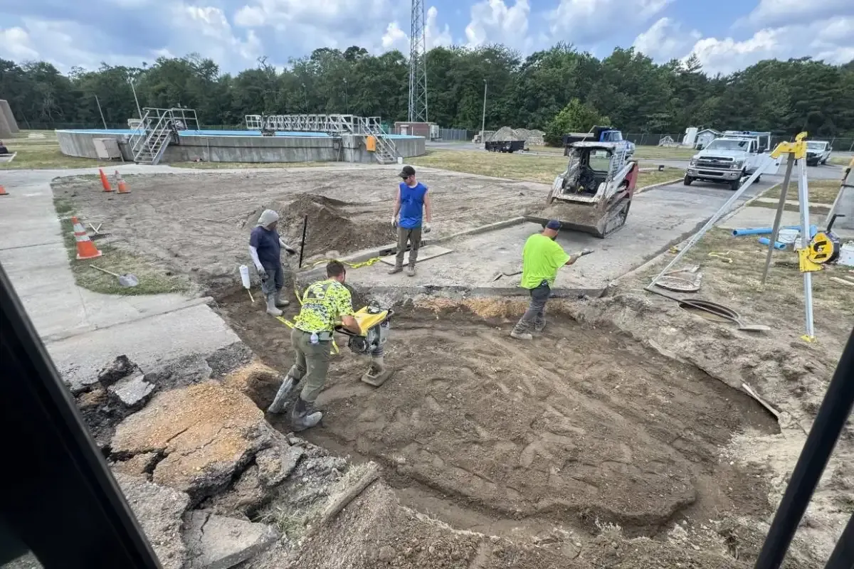 Crew compacting soil on a large commercial job site with equipment nearby