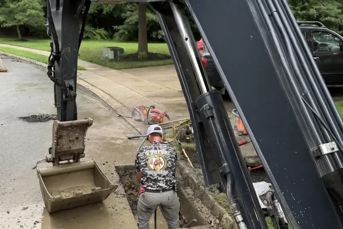 How Long Does Trenchless Pipe Bursting Take? Sewer Kings crew member guiding an excavator bucket at a small street side pit