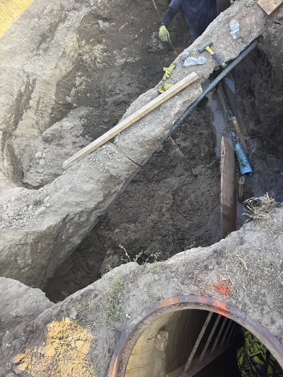 Open end of a large concrete pipe exposed at the bottom of a deep excavation