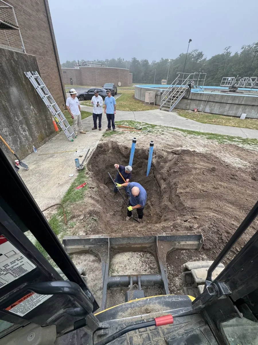 Crew working in a wide excavation at a commercial facility with pipes standing upright