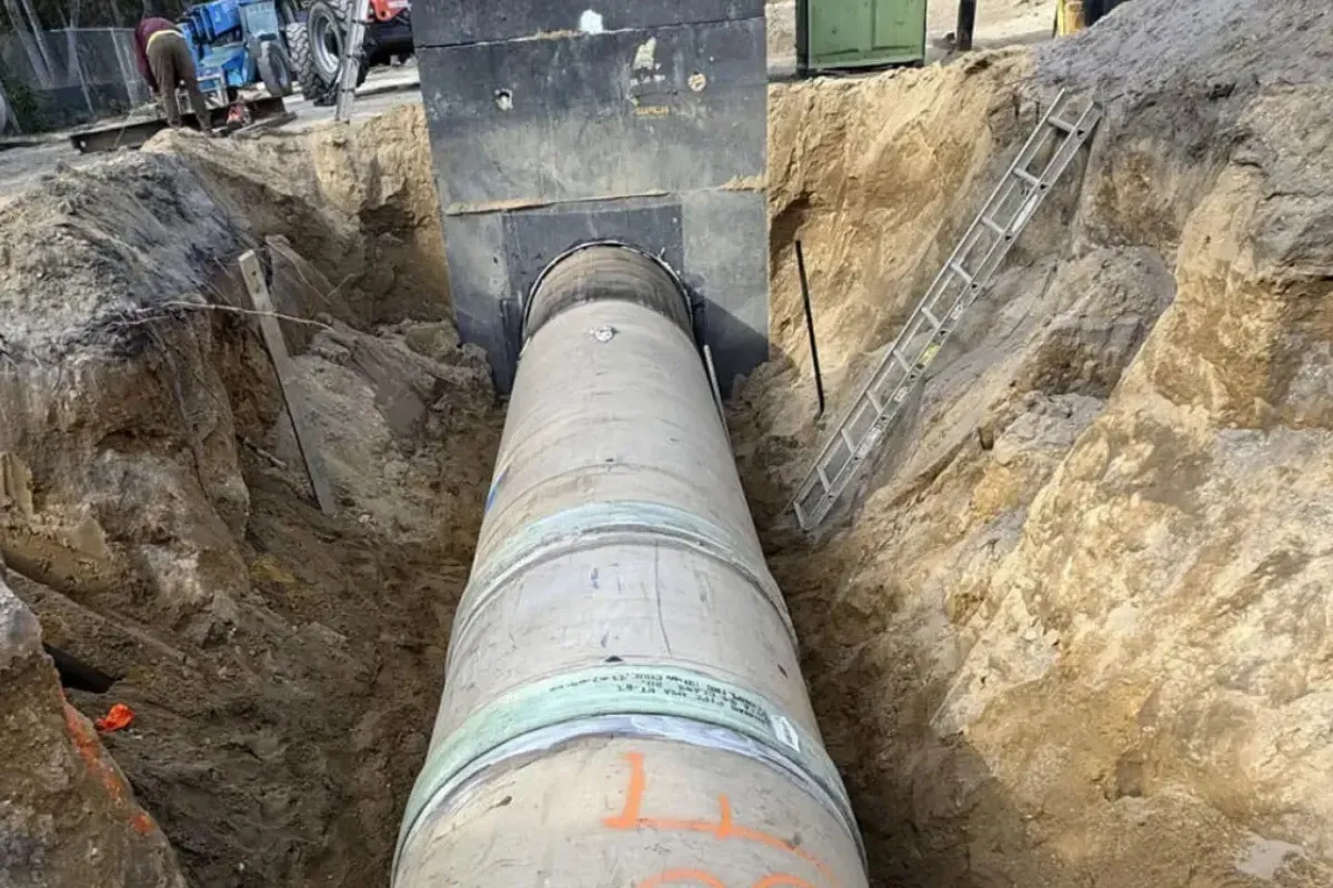 Large concrete pipe running through a deep trench with a ladder against the wall