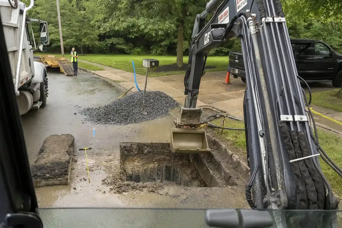 Mini excavator digging a small access pit at the curb of a residential street