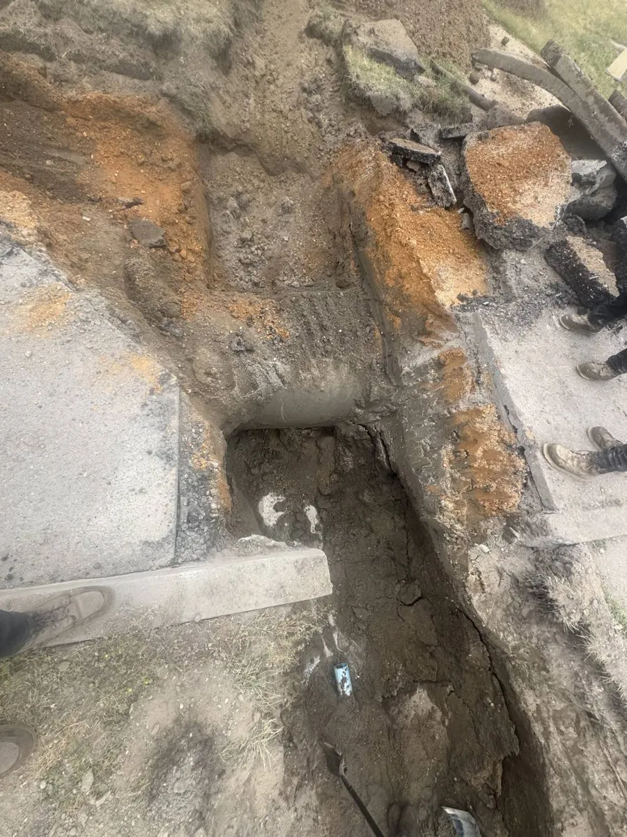 Narrow excavated pit with a buried pipe exposed at the bottom