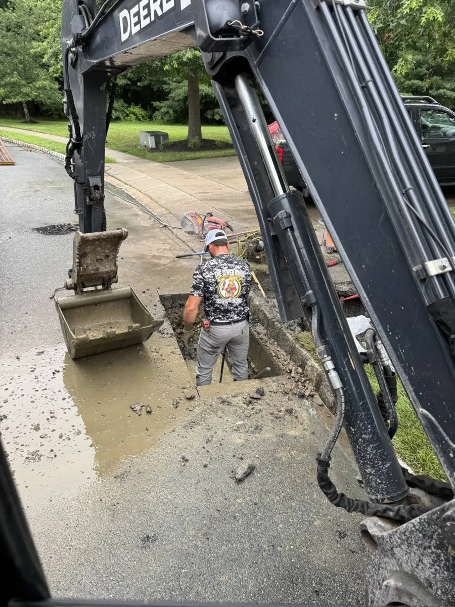 Is Trenchless Sewer Repair Worth the Extra Cost? Excavator arm and Sewer Kings crew member at an open dig on a wet residential street