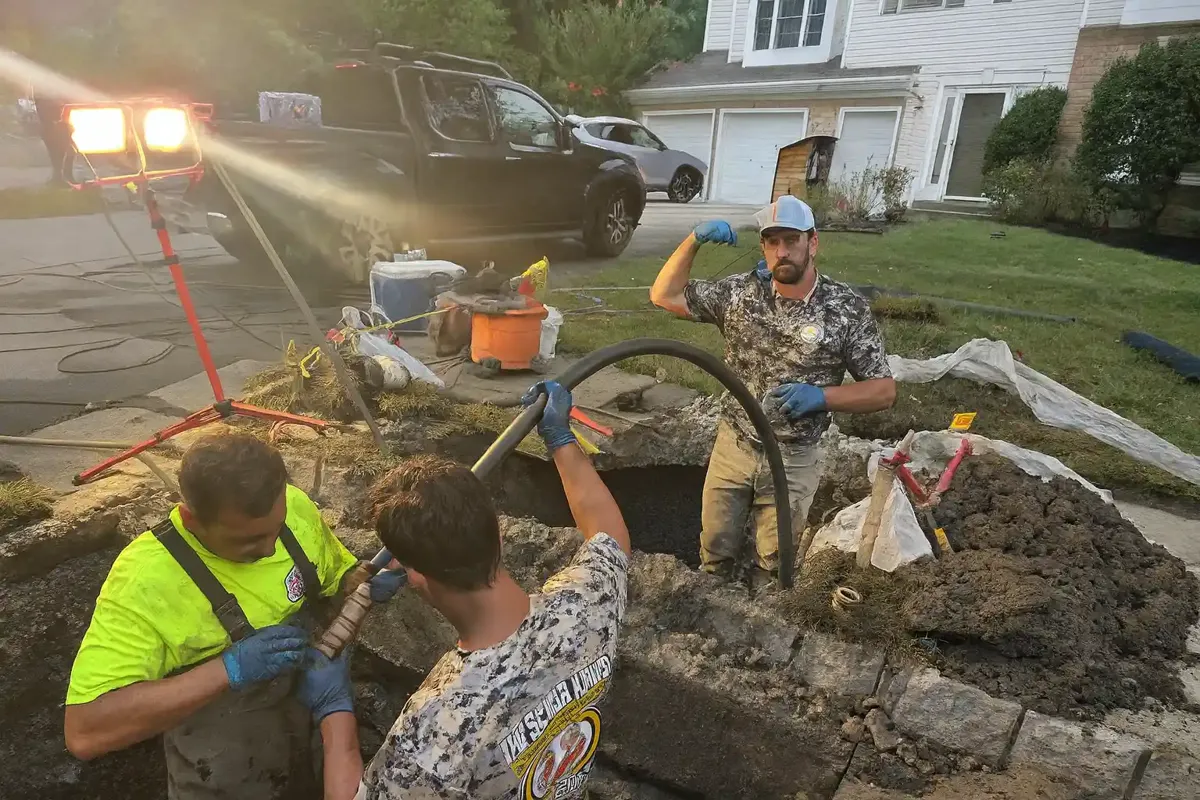 How Much Does Trenchless Sewer Line Replacement Cost? Sewer Kings crew working in a curbside pit under work lights at dusk