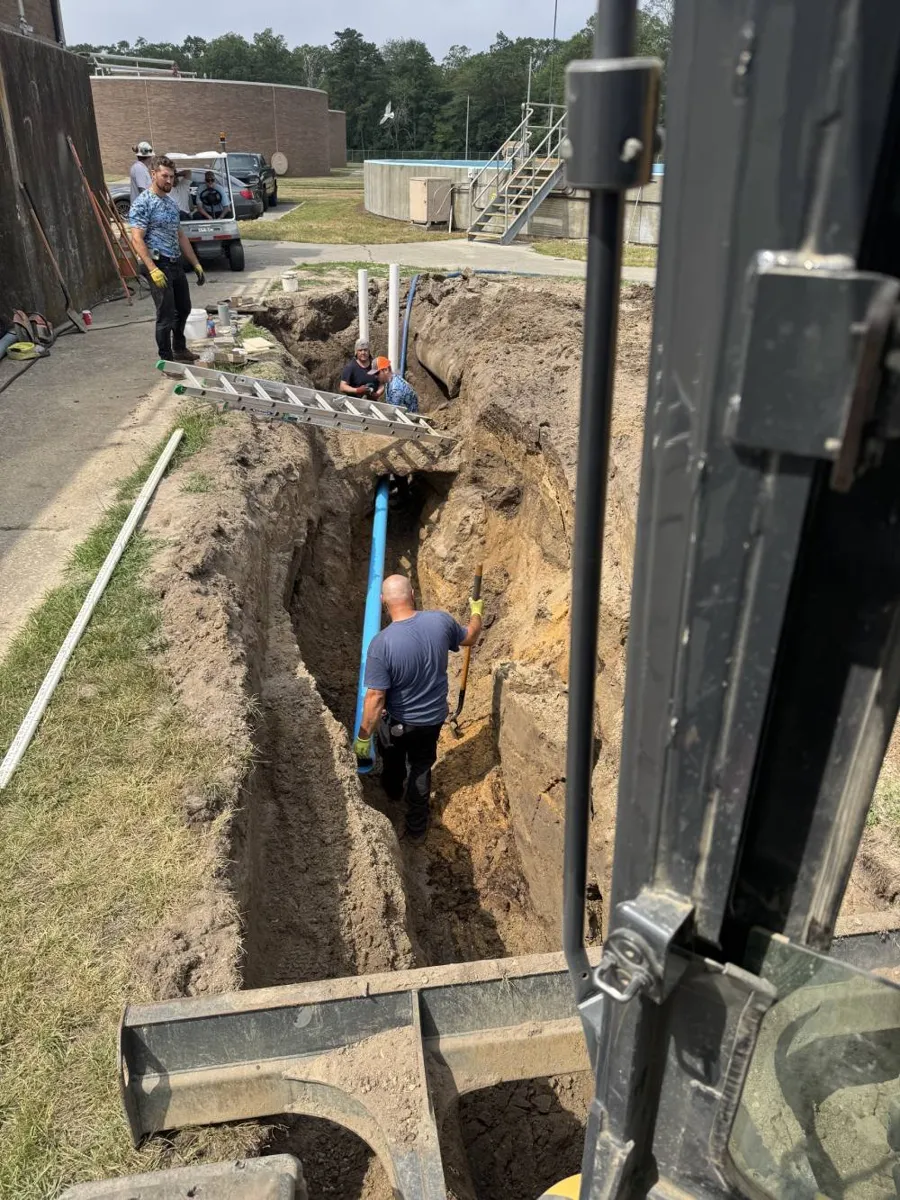 Can Trenchless Sewer Replacement Be Done in Winter? Crew member standing deep in a narrow trench beside a new blue pipe