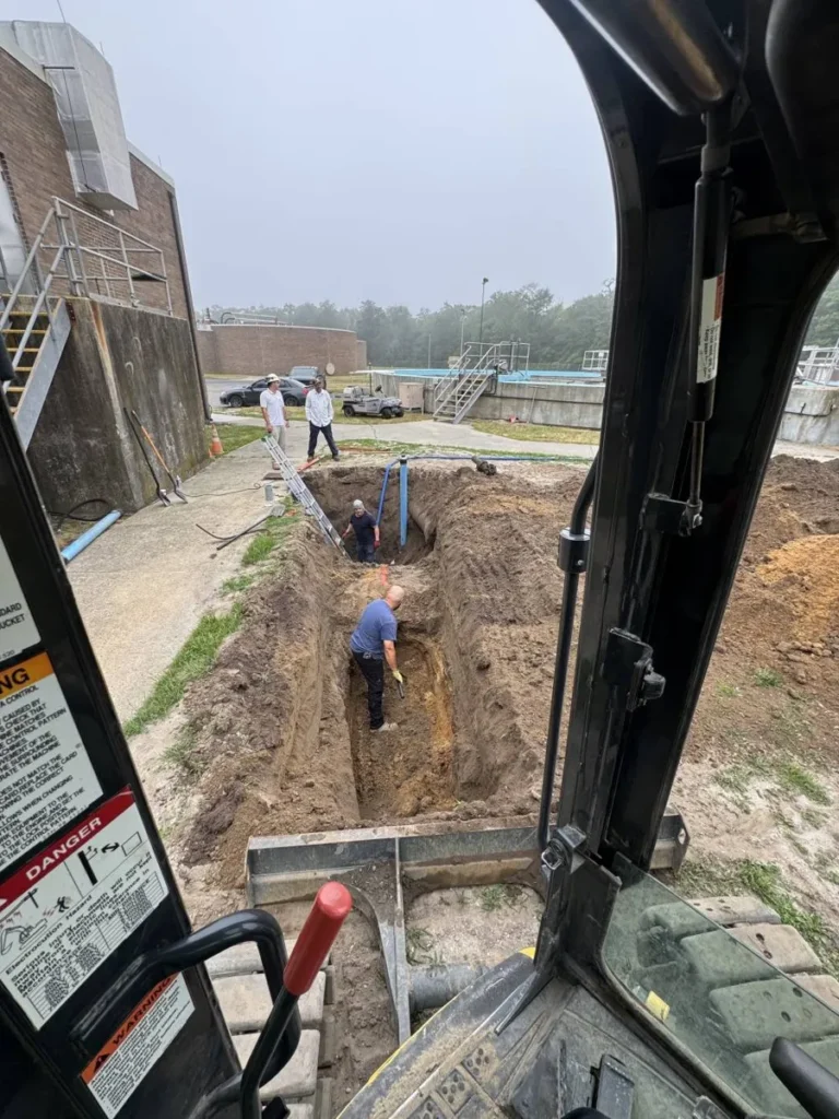 Can Trenchless Sewer Replacement Be Done in Winter? View from an excavator cab looking down into a narrow trench on an overcast day