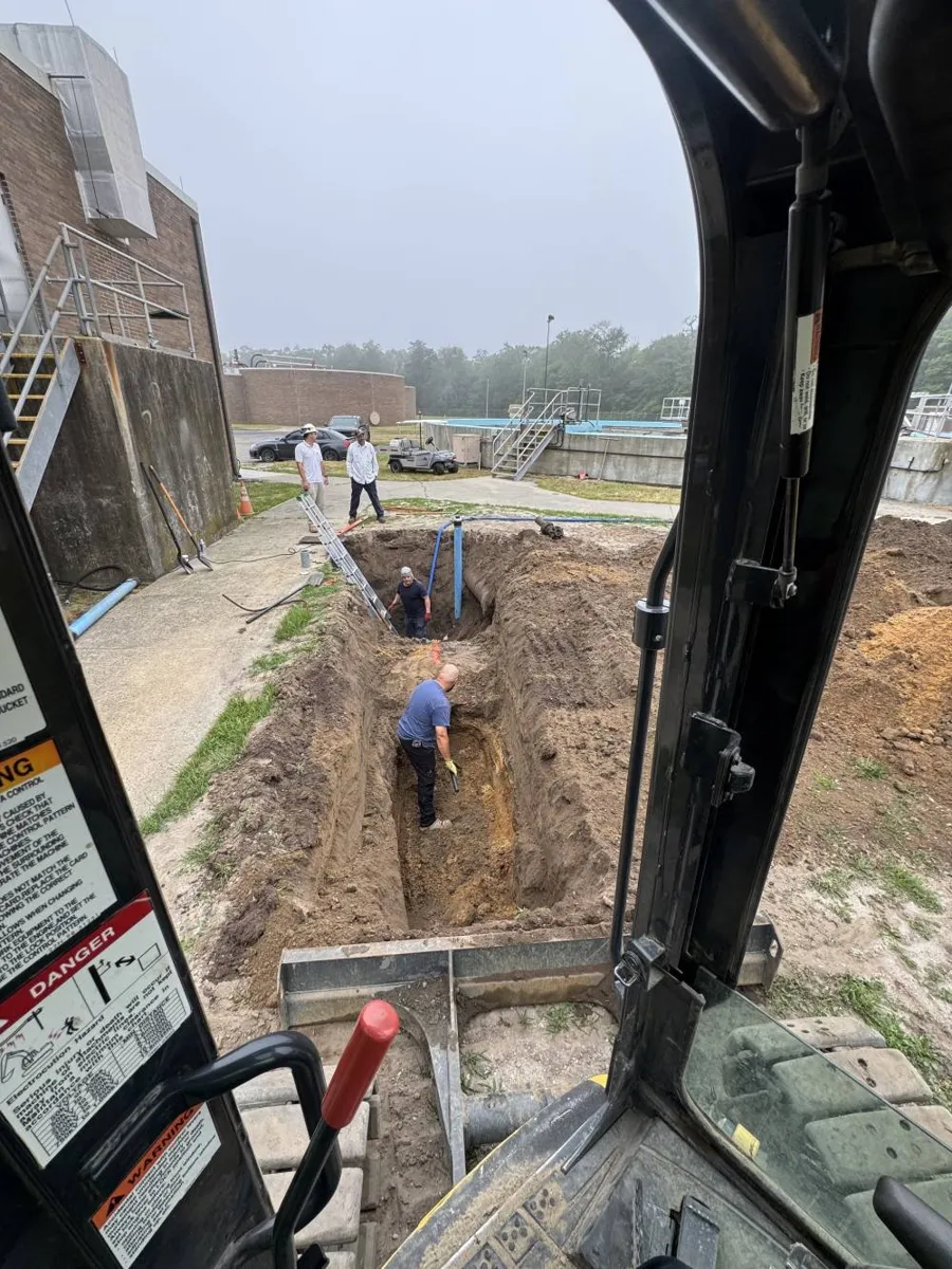 View from an excavator cab looking down into a narrow trench on an overcast day