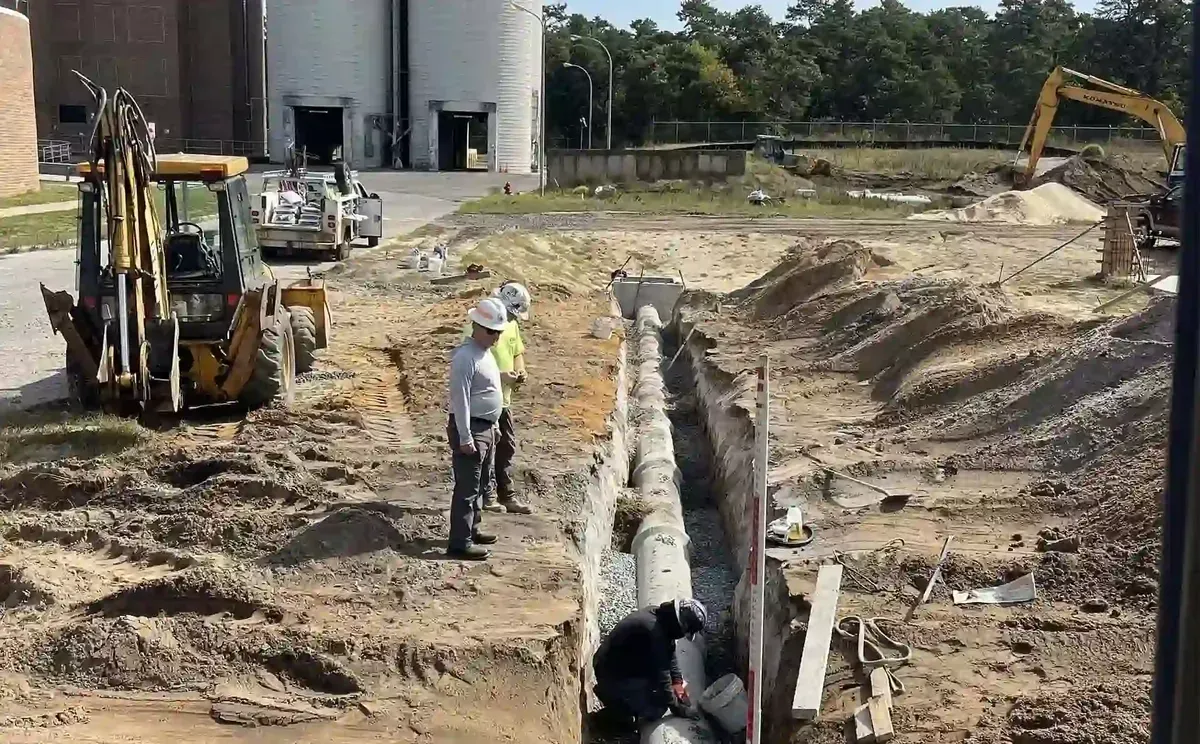 Trenchless Sewer Replacement vs. Traditional Dig-and-Replace Long open trench with pipe laid in it and a backhoe parked beside a commercial building