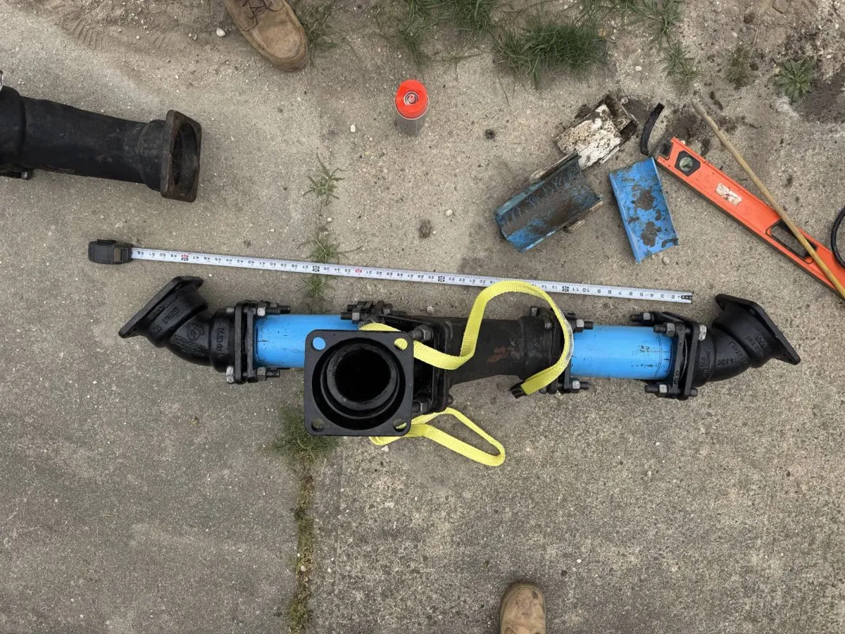 Why Is My Toilet Gurgling? Blue sewer pipe section with black cast iron fittings laid out on concrete beside a tape measure